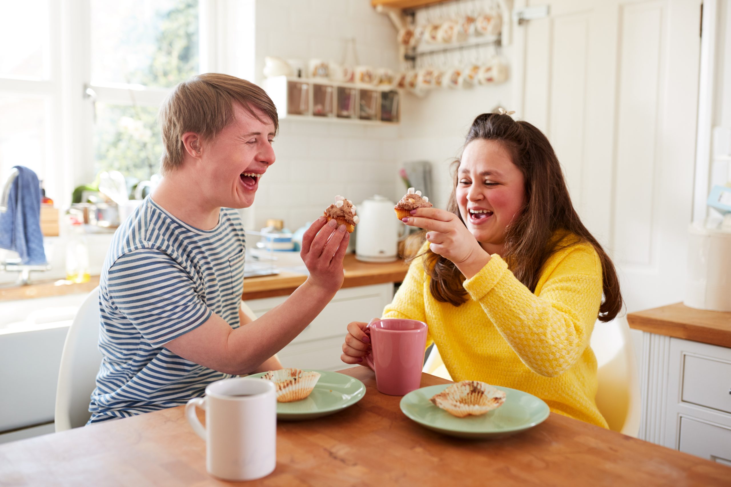 Young Downs Syndrome Couple Enjoying Tea And Cake In Kitchen At Home